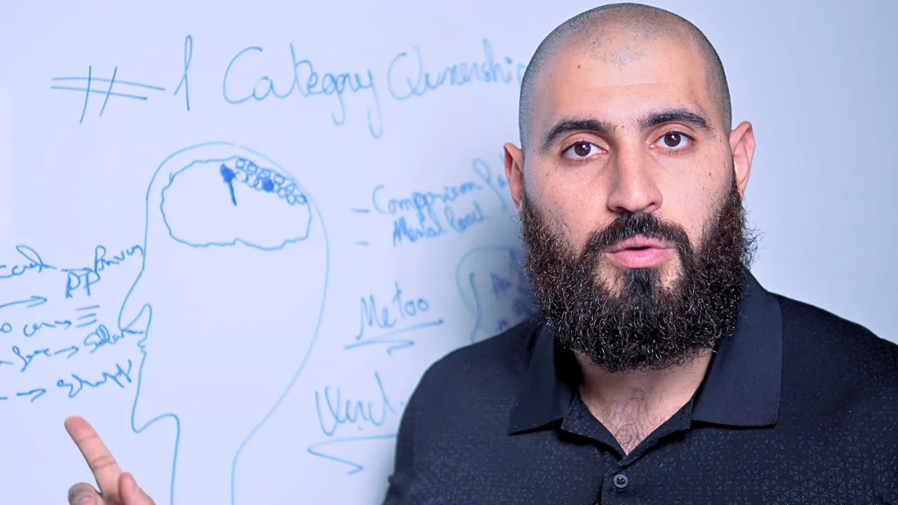 Bald, bearded man in a black polo points beside a whiteboard with a head-and-brain sketch and blue notes